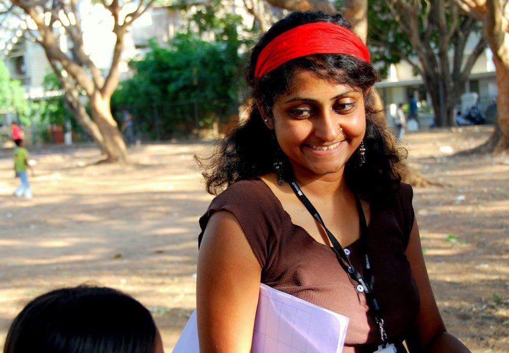 Nithya smiling at a small child while working in the field.