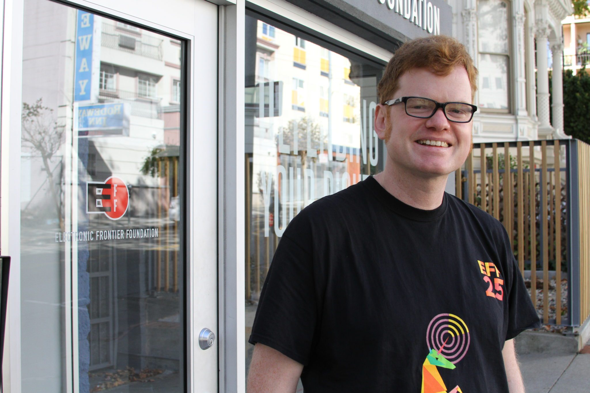 Elliot smiling, wearing a black shirt with a rainbow unicorn and the text 