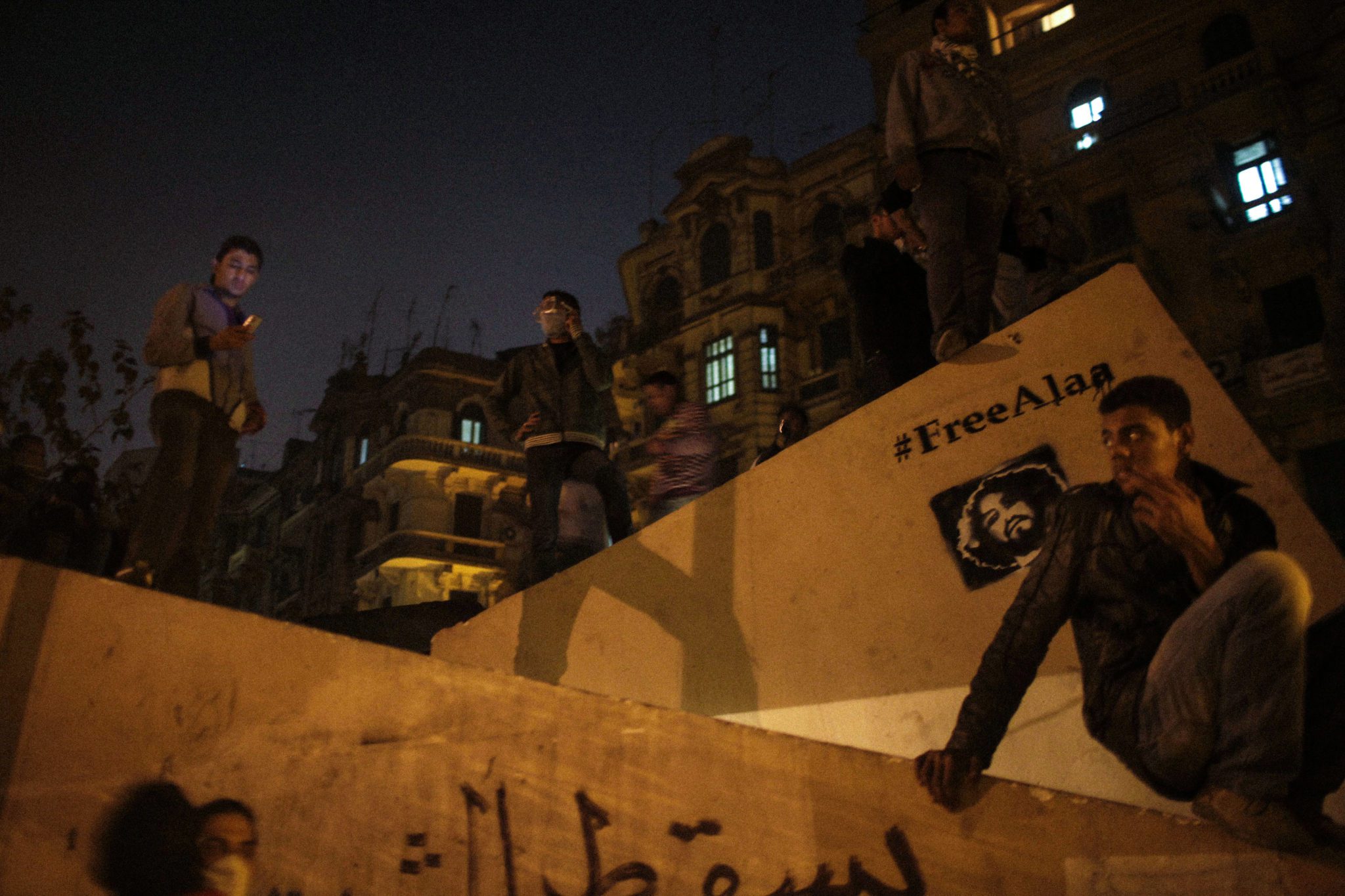 CAIRO, EGYPT - NOVEMBER 22:  Egyptian protesters look on from a raised structure during intense scuffles with police involving rocks, teargas, and molotov cocktails being thrown back and forth in the side streets near Tahrir Square in Cairo, Egypt on November 22, 2011. Graffiti is seen of political activist Alaa Abd El Fattah who was imprisoned the military for 
